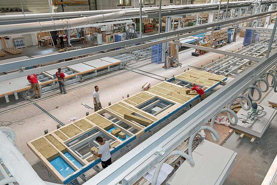 Workers producing prefabricated housing panels inside a factory